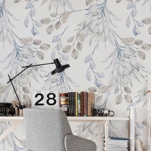 Può includere: Una scrivania bianca con una sedia grigia e un calendario che dice "28". La parete dietro la scrivania ha una stampa ad acquerello di foglie blu e grigie.