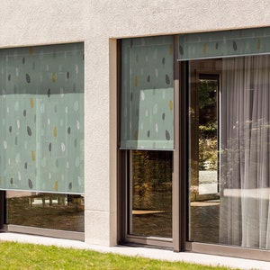 May include: Two windows with light green patterned roller shades. The shades have a leaf design. The windows are on a white wall.
