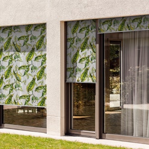 May include: Two windows with white exterior walls and green pea pod patterned roller shades. The shades are partially rolled up, revealing a view of a green lawn.