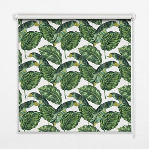 以下が含まれることがあります： 緑の熱帯の葉の模様がついた白いローラーシェード。葉はスタイリッシュで、薄い緑、濃い緑、黄色のカラーパレットを使用しています。