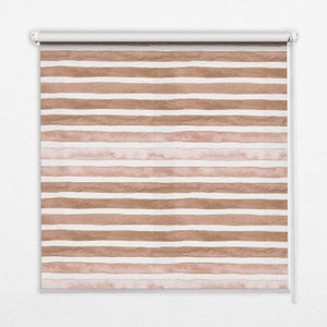 以下が含まれることがあります： 茶色とピンクの水彩画のストライプ模様が施された白いローラーシェードです。