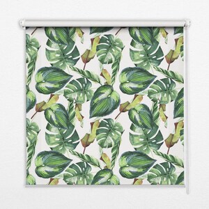 Może przedstawiać: Roleta z powtarzającym się wzorem akwarelowych liści tropikalnych w odcieniach zieleni, żółci i brązu na białym tle. Liście obejmują monsterę i inne tropikalne liście. Roleta jest zamontowana na białym mechanizmie rolkowym.