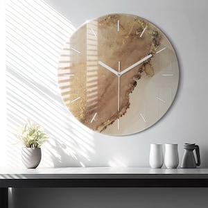 Può includere: Un orologio rotondo bianco con accenti dorati e un design marmoreo marrone. L'orologio ha lancette bianche e numeri neri.