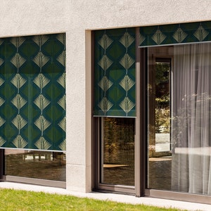 May include: Two windows with green and gold patterned roller shades. The shades are pulled down and the windows are closed. The windows are on a white building with a green lawn in front.