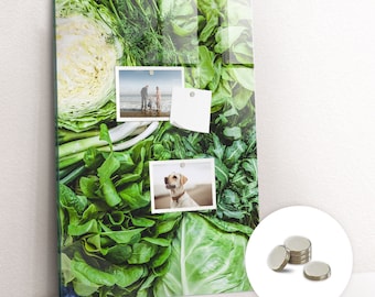 Puede incluir: Una pizarra magnética de vidrio con un fondo de verduras de hoja verde. La pizarra tiene dos fotos sujetas con imanes. Una foto muestra una familia de tres en una playa y la otra foto muestra un perro Labrador Retriever amarillo. La pizarra también tiene una nota adhesiva blanca sujeta con un imán.
