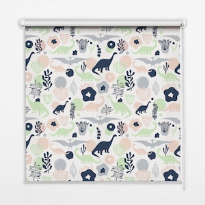 以下が含まれることがあります： 緑、青、ピンクの色合いの恐竜、花、葉の繰り返しパターンが施された白いローラーブラインドです。