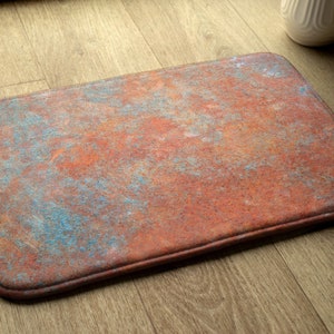 Puede incluir: Una alfombra rectangular de color óxido con un patrón de mármol azul y naranja. La alfombra tiene un borde cosido.