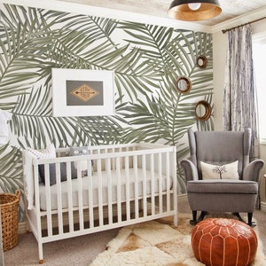 May include: A nursery room with a white crib, a gray rocking chair, and a brown leather pouf. The wall is covered in a tropical palm leaf wallpaper. A framed sign with the text "Stay True" is hanging on the wall.