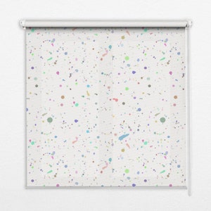 以下が含まれることがあります： カラフルな水玉模様の白いローラーブラインド。ブラインドは白地に、ピンク、ブルー、グリーン、イエロー、オレンジなど、さまざまな色の小さなカラフルなドットとペイントの飛び散りが施されています。