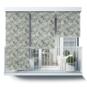 May include: White balcony with three white roller shades with a leafy pattern. The shades are partially rolled up, revealing a view of a balcony with a white railing, a white couch, a table and chairs, and potted plants.