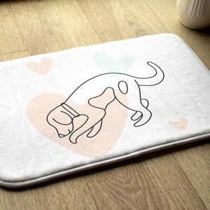 May include: White bath mat with a black line drawing of a dog with pink hearts on the mat.