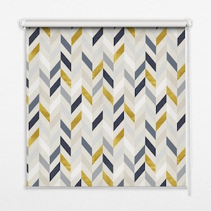 Może przedstawiać: Roleta z powtarzającym się wzorem w jodełkę. Wzór zawiera kolory złota, granatu, szarości i złamanej bieli. Roleta jest zamontowana na białym mechanizmie rolowania, przeznaczona do osłony okien.