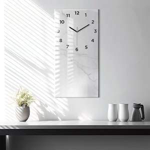May include: A white marble clock with black hands and black numbers. The clock is hanging on a white wall with a window behind it.