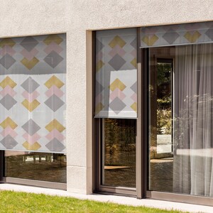 May include: Two windows with exterior roller shades featuring a geometric pattern of pink, gold, and gray squares. The shades are partially rolled down.