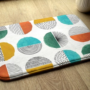 May include: A white bath mat with a repeating pattern of colorful circles. Each circle is divided into sections with different geometric patterns and colors, including teal, green, yellow, and orange.