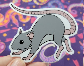May include: A gray rat sticker with a pink tail and pink feet. The sticker is on a purple background with a colorful pattern.