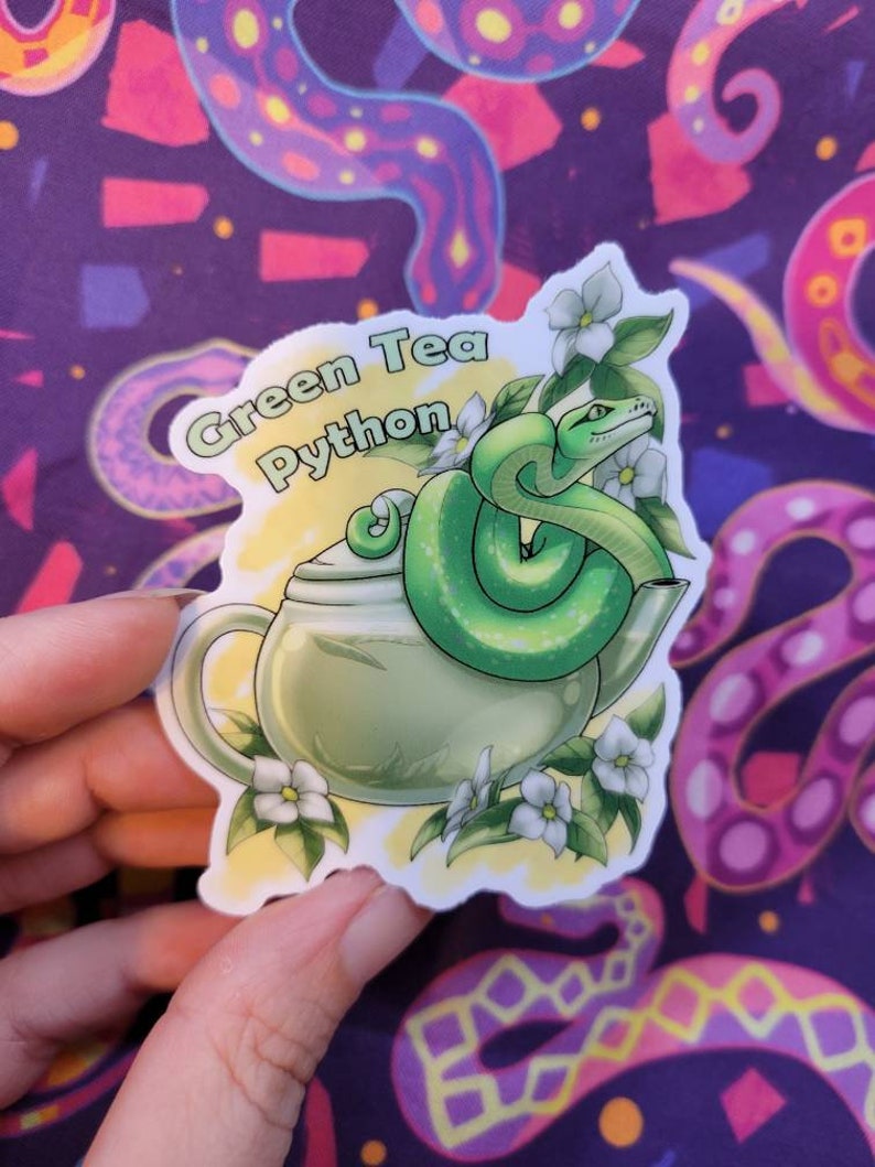 May include: Green Tea Python sticker featuring a green snake curled around a teapot with white flowers. The sticker has a yellow background with the text "Green Tea Python" in black.