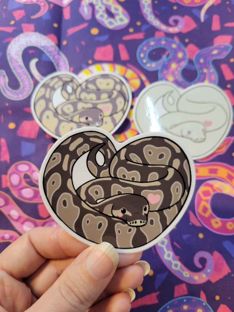 May include: A sticker of a brown and black snake curled up in a heart shape. The snake has a pink heart on its side and a cute cartoon face. The sticker is on a purple background with a pattern of colorful snakes.