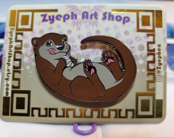 May include: A brown and white enamel pin of an otter curled up with a pink paw visible. The pin is on a beige background with gold accents and the text "Zyepht Art Shop" in purple.