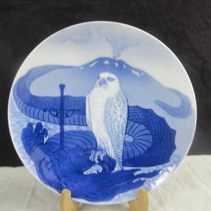 May include: A blue and white ceramic plate with a white bird and a blue mountain scene. The plate is oval shaped and has a raised rim.