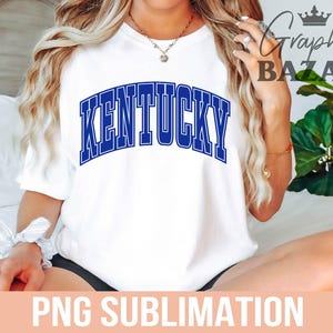May include: White t-shirt with the word "KENTUCKY" in blue, arched lettering. The shirt is a casual style, suitable for everyday wear. The image also includes the text "PNG SUBLIMATION".