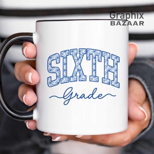 May include: A white ceramic mug with a black handle and rim. The front features the blue text SIXTH in a block font with a floral pattern, followed by the word Grade in a blue cursive script. The text Graphix BAZAAR appears in the top right.