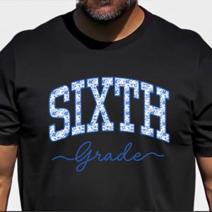 May include: A black short-sleeved t-shirt featuring the word SIXTH in large, block-style letters filled with a blue and white floral pattern, positioned above the word Grade written in a blue cursive script font across the center chest.