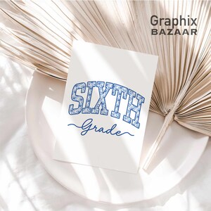 May include: A white rectangular card featuring the text SIXTH in a blue floral pattern block font, with the word Grade written below in a blue cursive script. The card is positioned on a white plate next to a large, dried, light beige palm leaf.