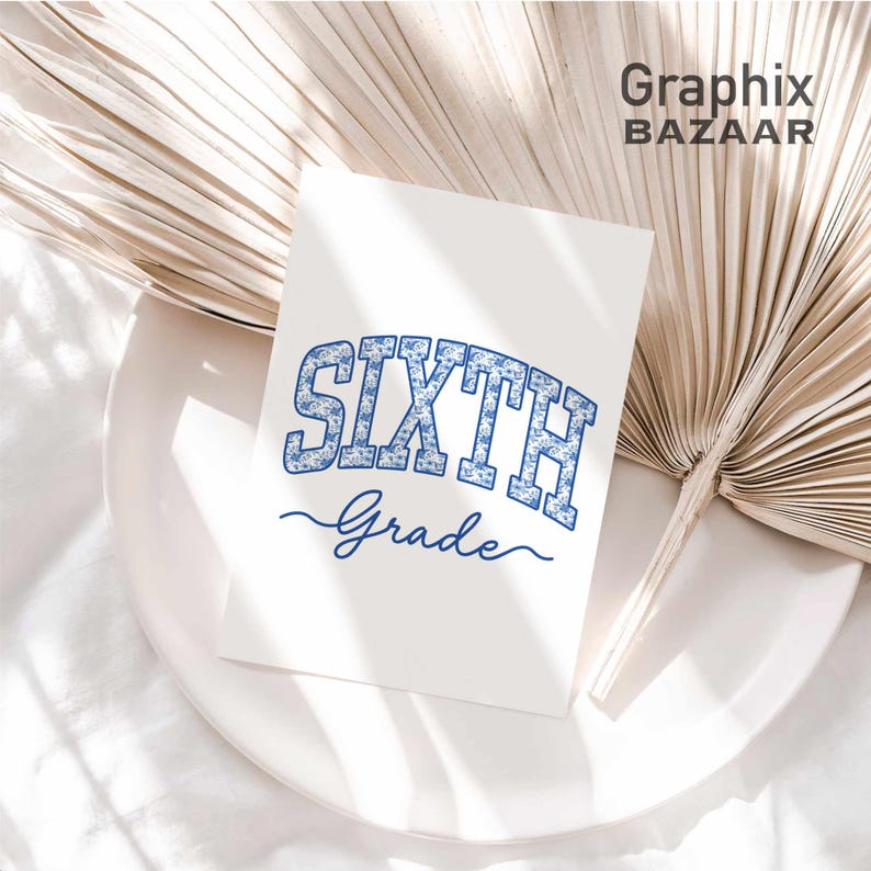 May include: A white rectangular card featuring the text SIXTH in a blue floral pattern block font, with the word Grade written below in a blue cursive script. The card is positioned on a white plate next to a large, dried, light beige palm leaf.