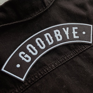 May include: A black denim jacket with a white embroidered patch that says "GOODBYE."