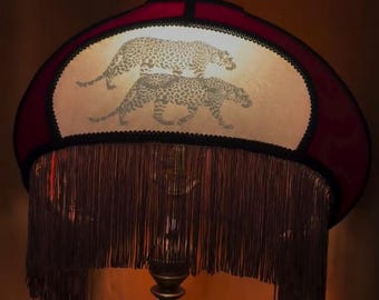 May include: A decorative table lamp with a burgundy shade featuring a leopard print design. The shade has a black trim and a fringe. The lamp has a brass base.
