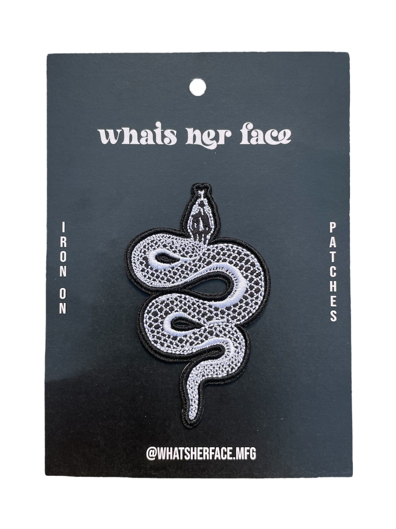 May include: Iron-on patch featuring a white snake with black outlines on a black background. The patch is packaged on a black card with the text "whats her face" and "@whatsherface.mfg".