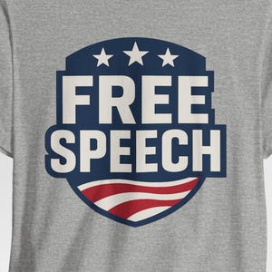 May include: A grey t-shirt with a navy blue and red graphic. The graphic displays the words "FREE SPEECH" in white, with three stars above and a red and white striped design below.