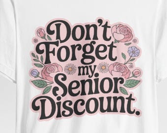 May include: White t-shirt featuring the phrase "Don't Forget my Senior Discount" in a retro font, with floral embellishments of pink roses, green leaves, and small blue and yellow flowers. The shirt is made of a soft material.