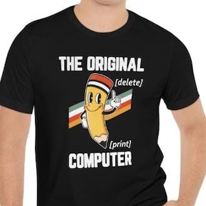 May include: Black t-shirt featuring the text "THE ORIGINAL COMPUTER" and a cartoon pencil design. The pencil has a red eraser and is holding a white rectangle with the words "delete" and "print".