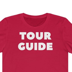 May include: Red short-sleeved t-shirt with the text "TOUR GUIDE" in white.
