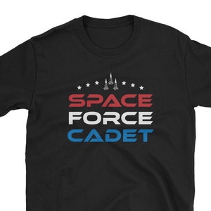 Könnte beinhalten: Schwarzes T-Shirt mit einer weißen, roten und blauen Grafik, auf der "SPACE FORCE CADET" mit Sternen und einem Raketenmotiv steht.