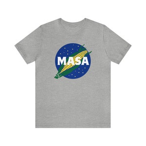 May include: A gray t-shirt with a blue circle and a corn cob graphic. The circle has white dots and the text "MASA" in white letters.