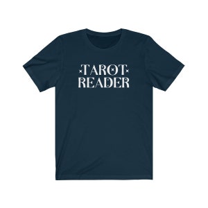 Op de afbeelding: Marineblauw T-shirt met de witte tekst "TAROT READER" in een schreeflettertype. De tekst is gecentreerd en bevat steraccenten. Het shirt heeft korte mouwen en een ronde hals.