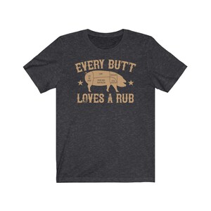 May include: Dark heather grey t-shirt with a brown graphic of a pig with a diagram of its cuts. The text "EVERY BUTT LOVES A RUB" is printed below the pig.