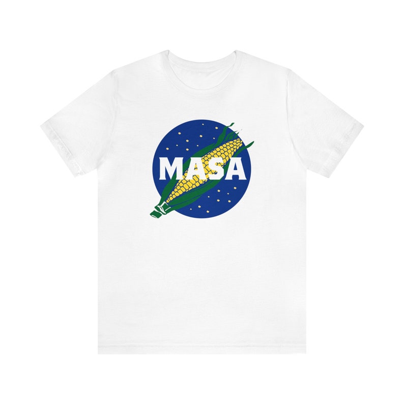 May include: White t-shirt with a blue circle and a corn cob graphic. The text "MASA" is printed in white letters inside the circle.