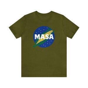 May include: A green t-shirt with a blue and white circle graphic featuring a corn cob and the word "MASA" in white letters.
