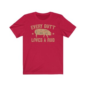 May include: Red short-sleeved t-shirt with a tan pig illustration and the text "EVERY BUTT LOVES A RUB".