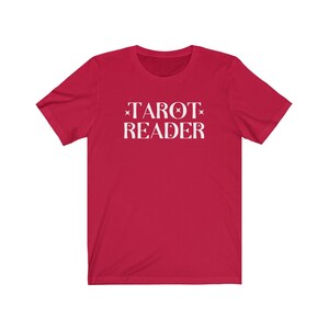 Op de afbeelding: Een rood t-shirt met de witte tekst "TAROT READER" in een gestileerd lettertype. De tekst is gecentreerd op de voorkant van het shirt. Het shirt heeft korte mouwen en een ronde hals.