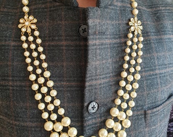 May include: A three-strand pearl necklace with gold accents and floral embellishments. The necklace is made of white pearls and has a gold chain.