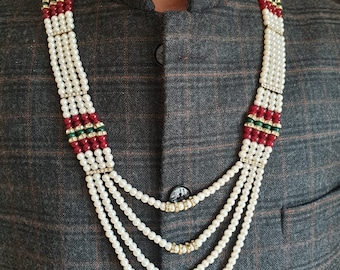 May include: A multi-strand necklace featuring white faux pearls, red beads, and green beads arranged in a layered design. The strands are accented with small gold-toned spacers embedded with clear crystals, creating a structured, tiered appearance.