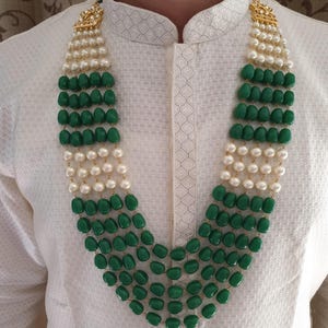 Pode incluir: Um colar de v&aacute;rias voltas com contas verdes e brancas. O colar tem um fecho dourado e est&aacute; sendo usado por uma pessoa.