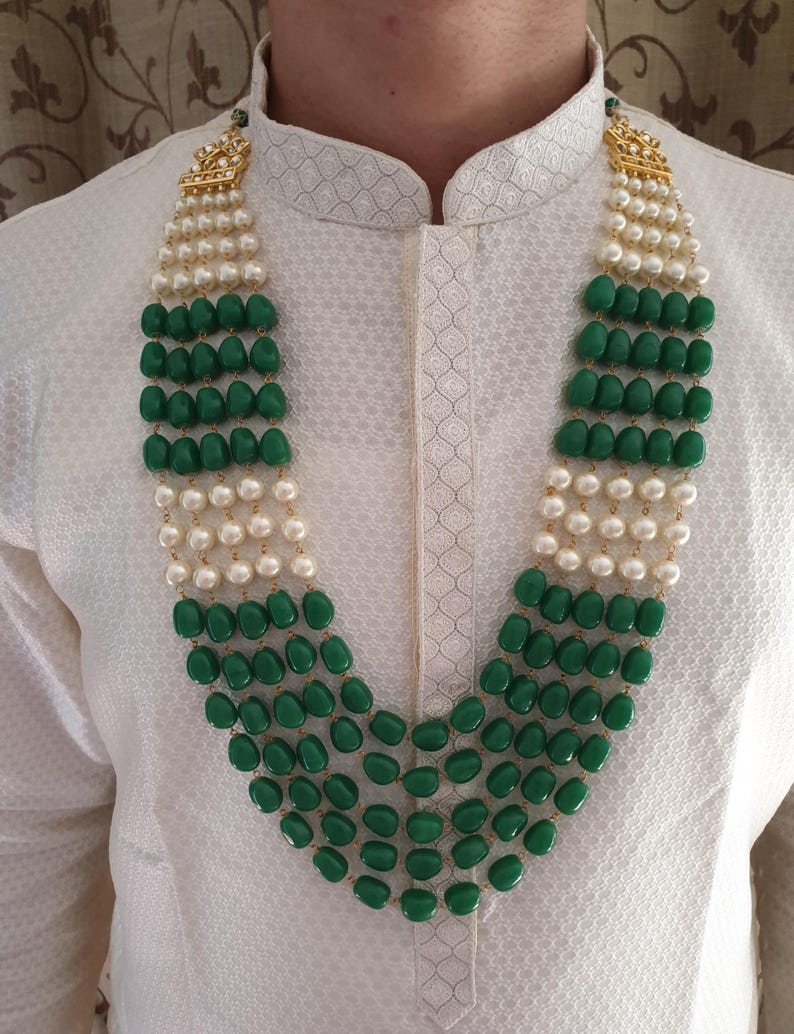 Pode incluir: Um colar de v&aacute;rias voltas com contas verdes e brancas. O colar tem um fecho dourado e est&aacute; sendo usado por uma pessoa.