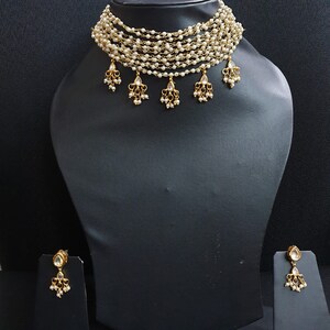 May include: A gold multi-strand pearl choker necklace with dangling pearl and clear stone accents. Matching earrings with pearl and clear stone accents.