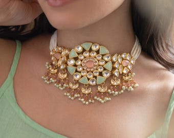 May include: A gold-toned choker necklace featuring a large central circular pendant with mint green and peach-colored stones. The piece includes multiple strands of small white beads and dangling accents with tiny pink and white beads along the bottom edge.